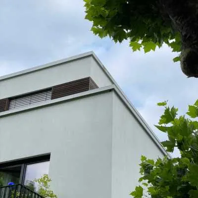 Hellgraue Putzfassade eines Einfamilienhauses mit anthrazitfarbenem Sockel