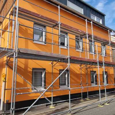 Eingerüstetes Stadthaus mit kräftig oranger Putzfassade und dunklem Sockel