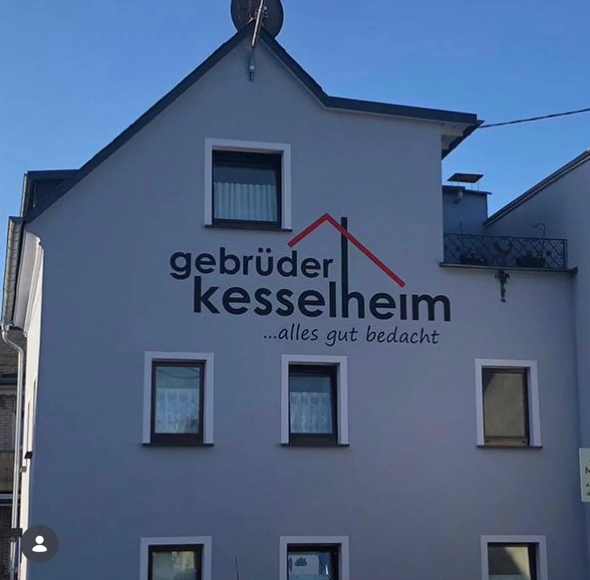 Graue Giebelfassade der Dachdeckerei Gebrüder Kesselheim mit handgemaltem Schriftzug und rotem Dach-Logo